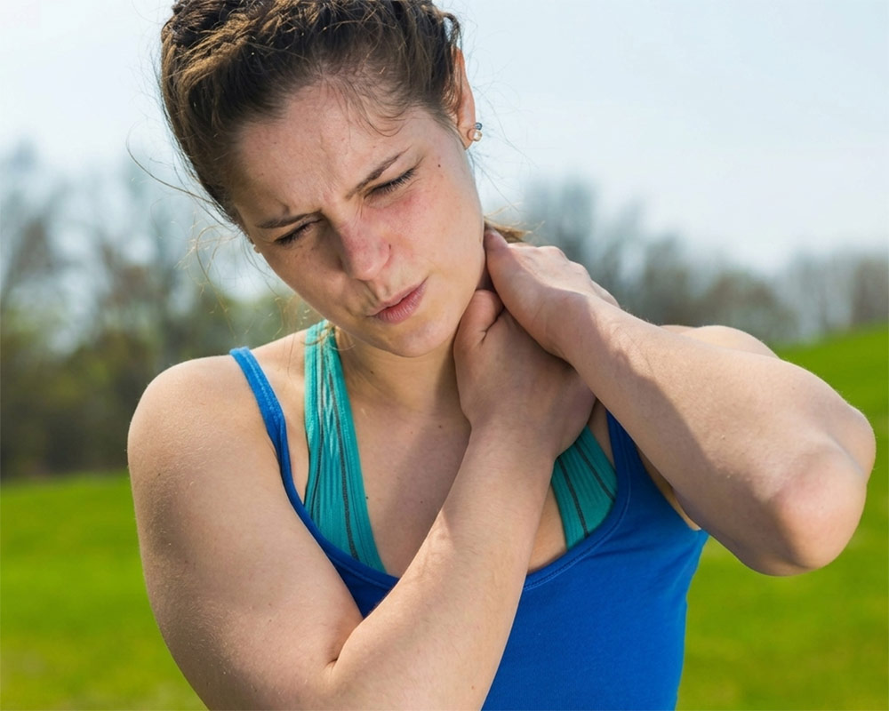 woman with shoulder pain after running A female runner outdoors gripping her sore neck and shoulder muscle, illustrating upper-body posture stiffness treated by mobile sports massage in York.