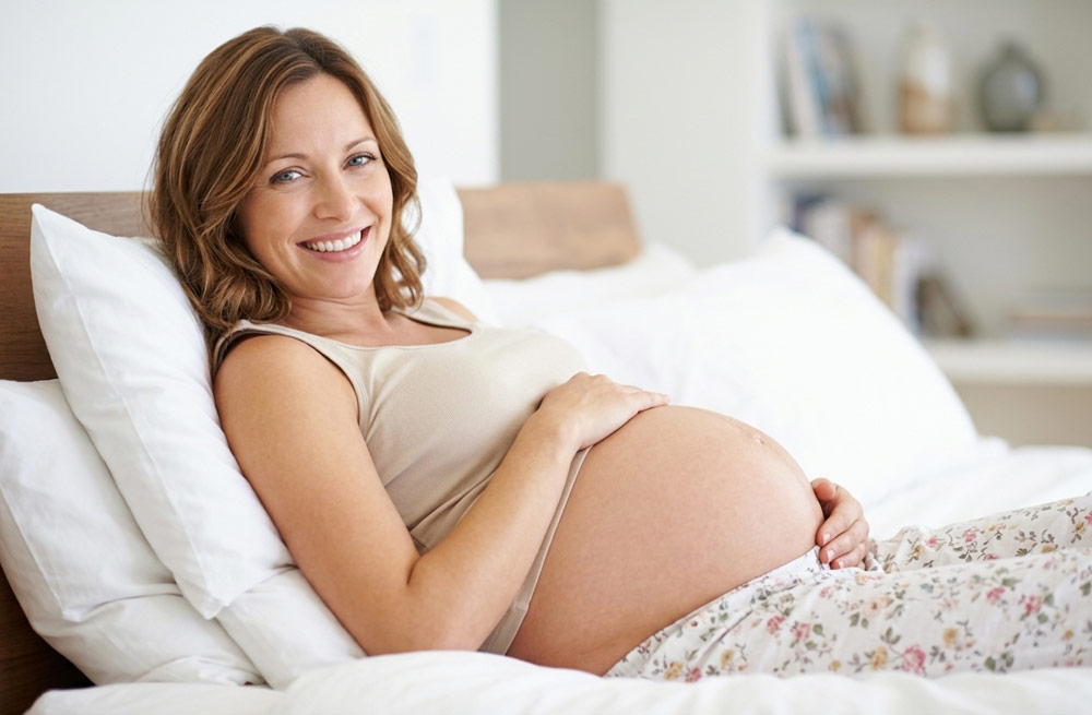 Smiling pregnant woman resting comfortably in bed, showcasing the relaxation and stress relief benefits of pregnancy massage in York.