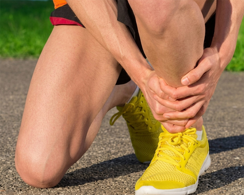 man with shin pain after running A runner kneeling on a path holding their painful lower leg and shin, illustrating running injury recovery with mobile sports massage in York.