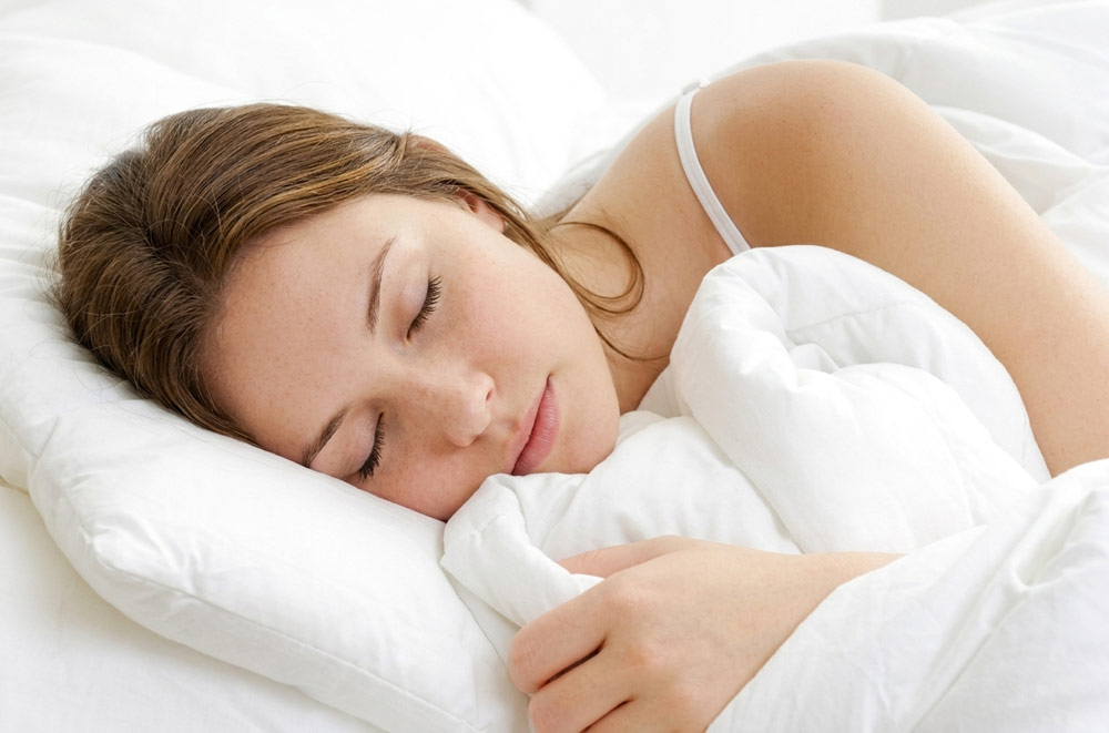 Woman sleeping deeply and peacefully in bed, demonstrating the improved sleep quality resulting from mobile postnatal massage in York