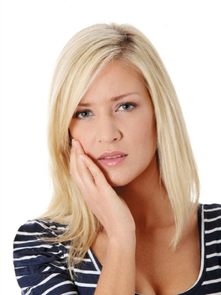 Blonde woman holding her cheek in discomfort, illustrating TMJ jaw pain and teeth grinding symptoms treated with mobile sports massage in York