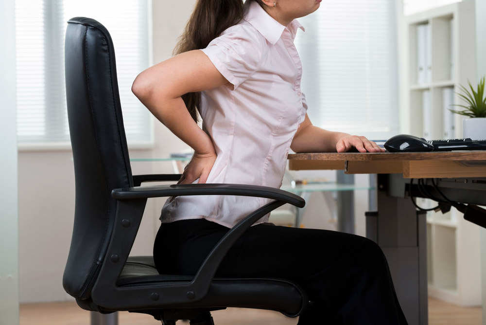 Woman sitting on a gym mat holding her lower back in pain, illustrating a weight training injury that requires assessment from a York sports massage and personal training specialist.